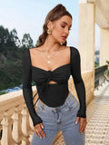 Woman in a black long-sleeve cropped top with a square neckline and tie detail, posing outdoors.