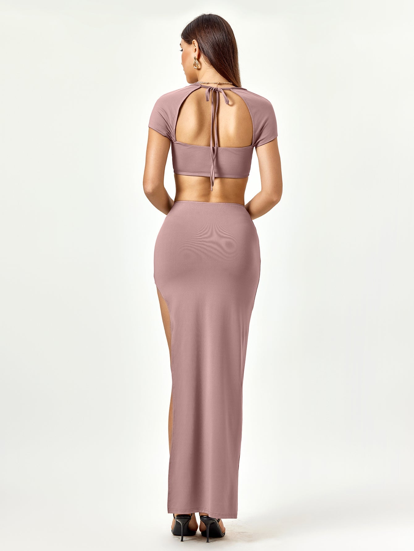 Back view of a woman in a mauve two-piece set featuring a cropped top with a tie closure and a high slit maxi skirt.