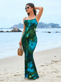 Woman holding a woven bag while wearing a green and blue tie-dye spaghetti strap mermaid maxi dress on the beach