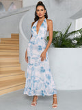 Full-length shot of a woman in a blue and white tie-dye print maxi dress with a plunging V-neck and halter straps, standing on a modern staircase.