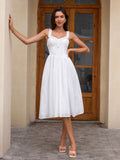 Woman in a white eyelet A-line midi dress with ruffled straps and a sweetheart neckline, posing with hands on hips.