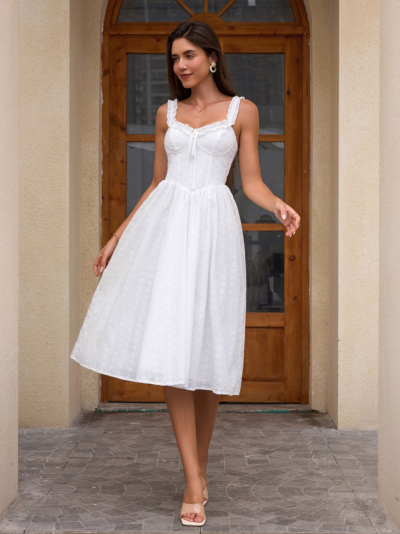 Woman wearing a white eyelet A-line midi dress with ruffled straps and a sweetheart neckline, standing outdoors.