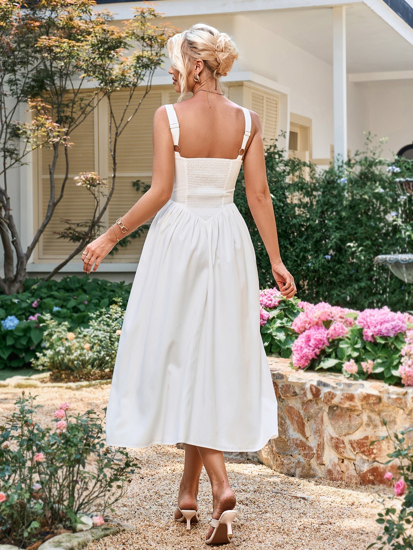 back view of a woman in a white sleeveless midi dress with a smocked back panel and full skirt