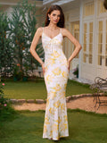 Full-body shot of a woman modeling a white maxi slip dress with a yellow floral print and lace trim, in a garden.