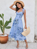 Woman wearing a blue floral print midi dress, straw hat, and carrying a straw bag.