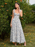 Woman wearing a blue and white floral print midi dress with a sweetheart neckline and tie shoulder straps, standing in front of an orange tree.