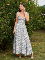 Woman wearing a blue and white floral print midi dress with a sweetheart neckline and tie shoulder straps, standing in front of an orange tree.