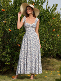 Woman wearing a straw hat and a floral print midi dress with a sweetheart neckline and tie shoulder straps, standing in front of an orange tree.