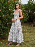 Woman in a blue and white floral print midi dress with a sweetheart neckline and tie shoulder straps, posing in an outdoor setting.