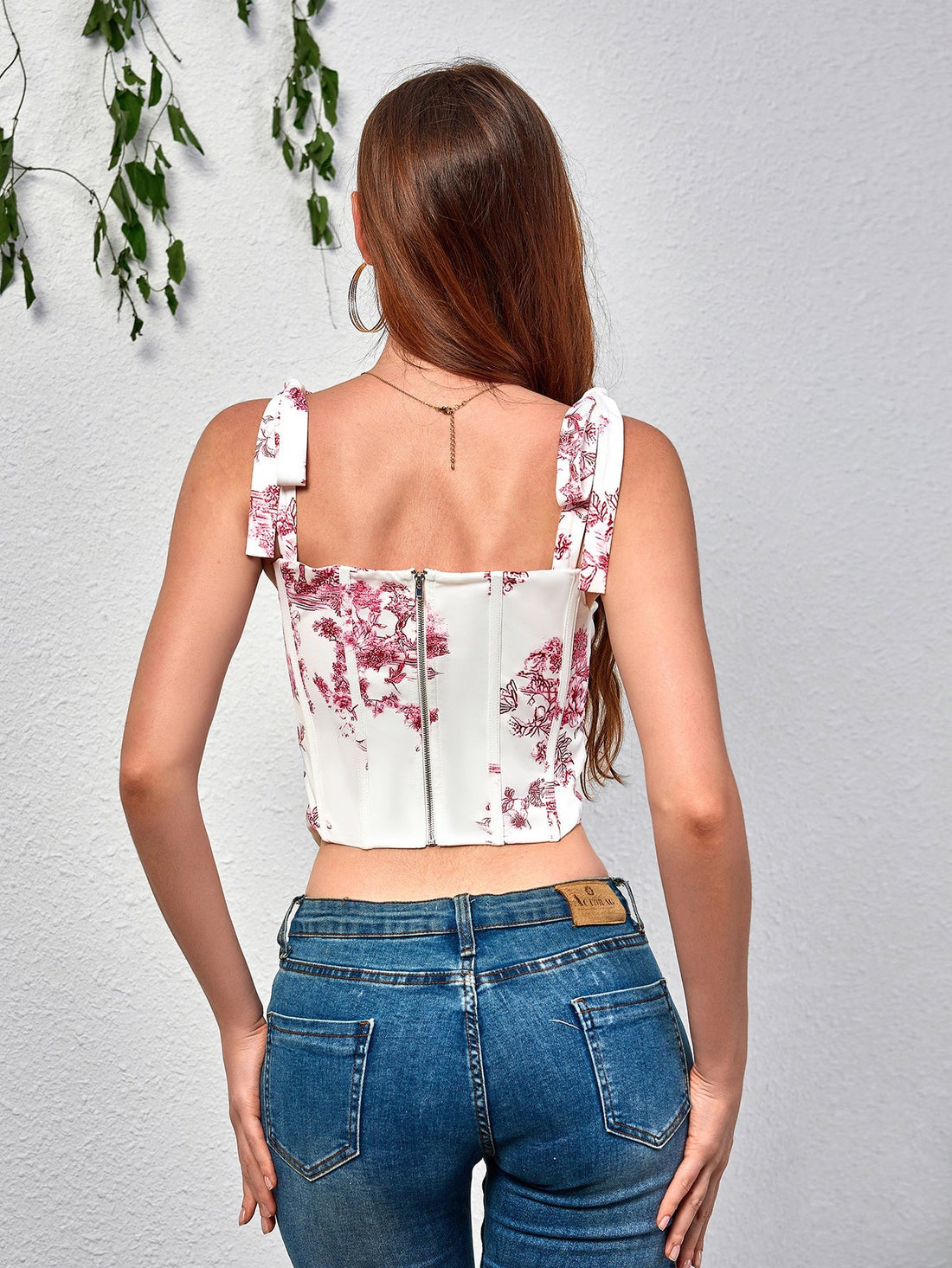 Woman wearing a white and red toile print corset top with tie straps and blue jeans