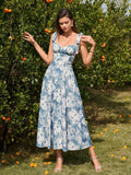 Woman adjusting her shoulder tie on a blue and white floral print midi dress in an orchard.