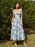 Woman wearing a blue and white floral print midi dress with tie shoulder straps, standing in an orchard.