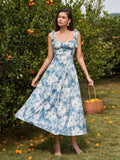 Woman in a blue and white floral print midi dress holding a basket of oranges.