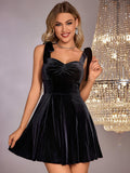Woman smiling and holding the hem of her black velvet fit and flare dress with bow shoulder straps.
