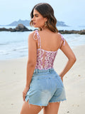 Rear view of a woman in a pink floral lace cropped camisole with tie straps and blue distressed denim shorts on a beach.