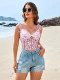 Woman wearing a pink floral lace cropped camisole with tie straps and blue distressed denim shorts on a beach.