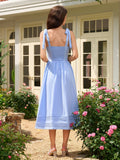 Back view of a woman in a light blue midi dress with smocked back detail and tie shoulder straps.