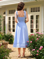 Back view of a woman in a light blue midi dress with smocked back detail and tie shoulder straps.
