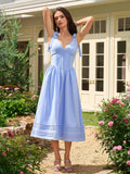 Woman in a light blue midi dress with tie shoulder straps, raising her arms in a garden.
