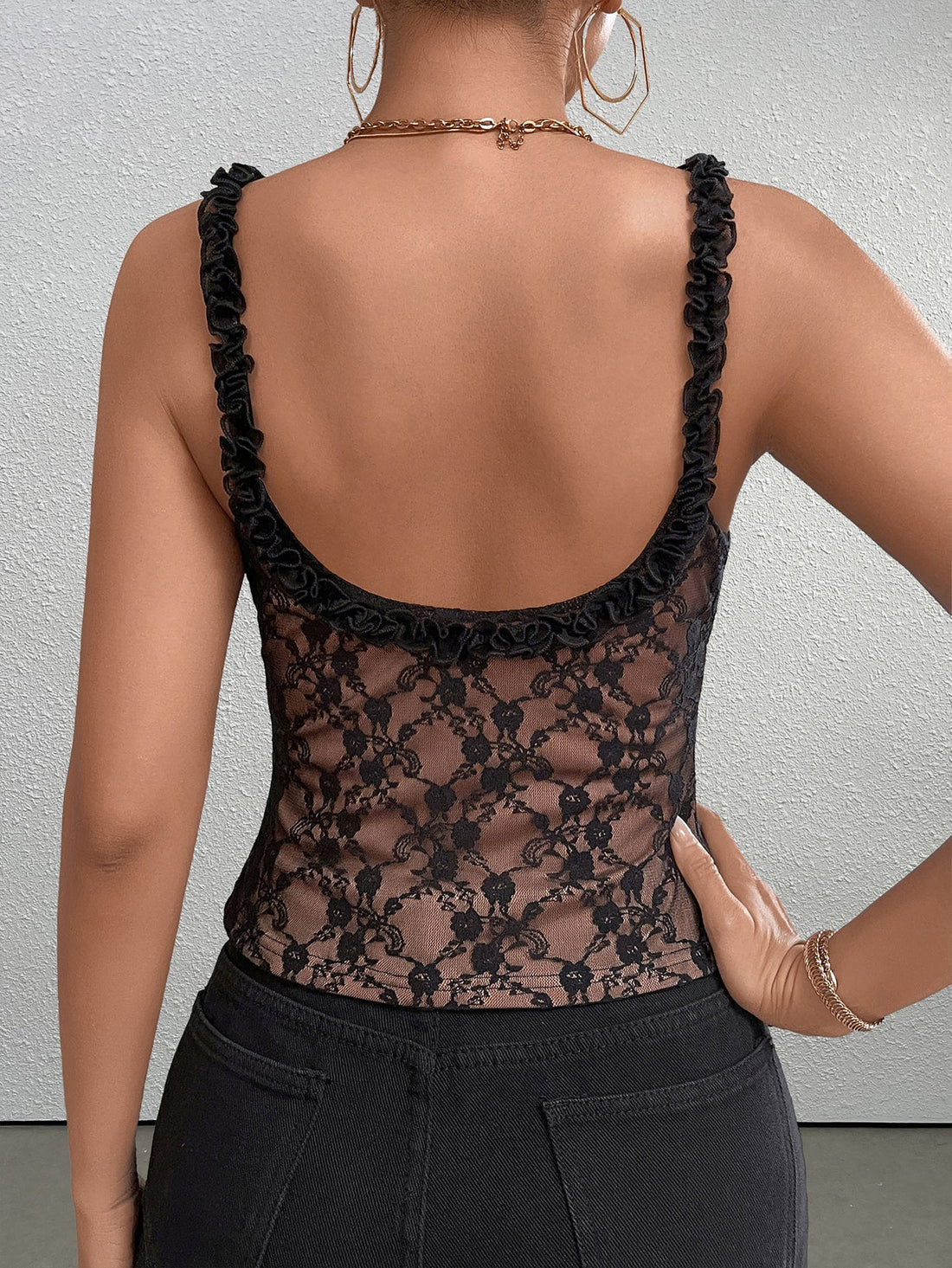 Woman wearing a black lace camisole with ruffled straps and a bow detail.