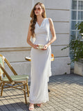 Woman in a long white sleeveless formal dress with a draped cowl neckline and flowing cape detail standing outdoors holding a teacup.
