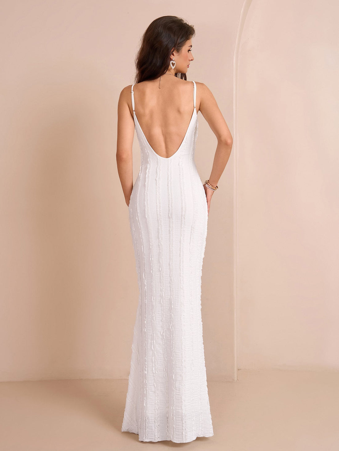 Woman wearing a white floor-length mermaid dress with spaghetti straps and diagonal textured detailing.