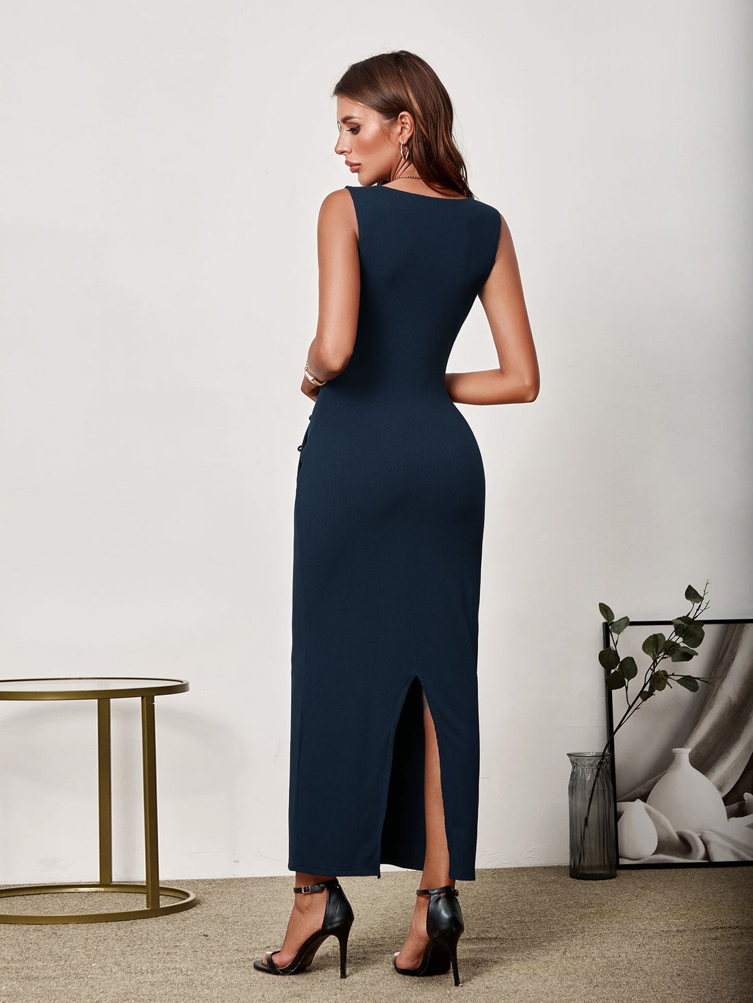 Woman wearing a navy blue sleeveless V-neck maxi sheath dress with button detailing and a side slit.