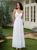 Woman wearing a white tiered maxi dress with spaghetti straps, with her hands clasped behind her back.