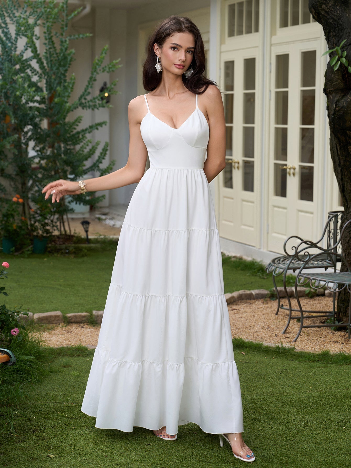 Woman in a white tiered maxi dress with spaghetti straps and a plunging neckline, with her hand on her hip.