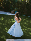 Woman in a light blue halter neck midi dress with a full skirt, posing outdoors in a garden.
