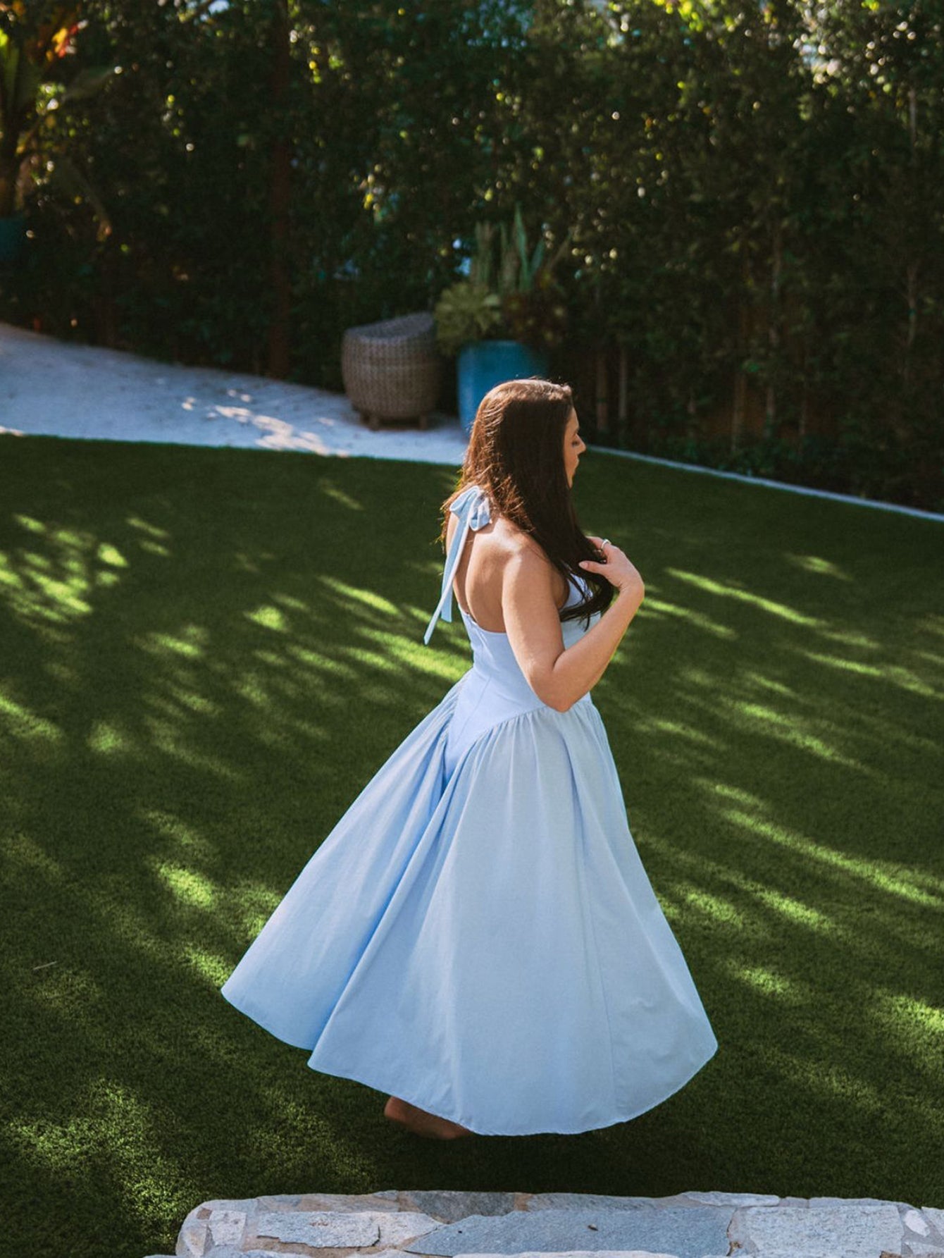 Woman in a light blue halter neck midi dress with a full skirt, posing outdoors in a garden.