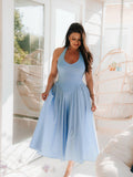 Woman in a light blue halter neck midi dress with a full skirt, standing indoors near a large window.