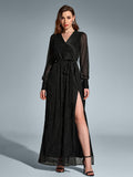 Front view of a woman in a black long-sleeved maxi dress with a v-neck and high slit, adorned with scattered metallic dots, standing with legs apart.