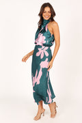 Woman posing in a green satin floral print halter dress, viewed from the side.