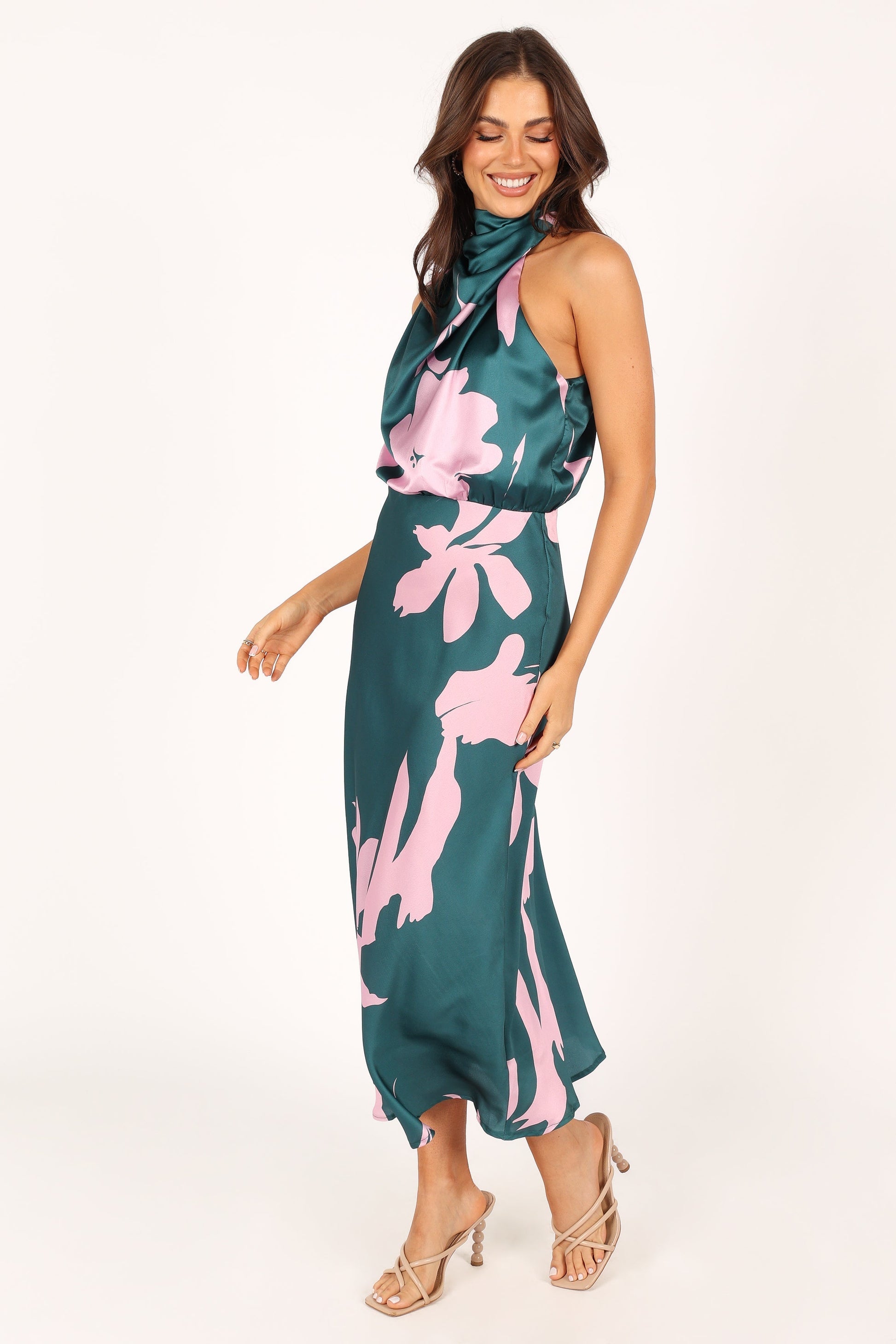 Woman posing in a green satin floral print halter dress, viewed from the side.