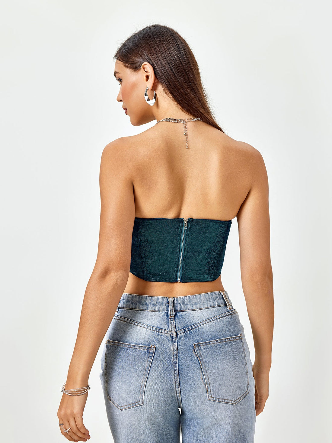 Woman wearing a teal textured metallic strapless corset top and light wash denim jeans