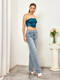 Full body shot of a woman in a teal textured metallic strapless corset top and light wash denim jeans