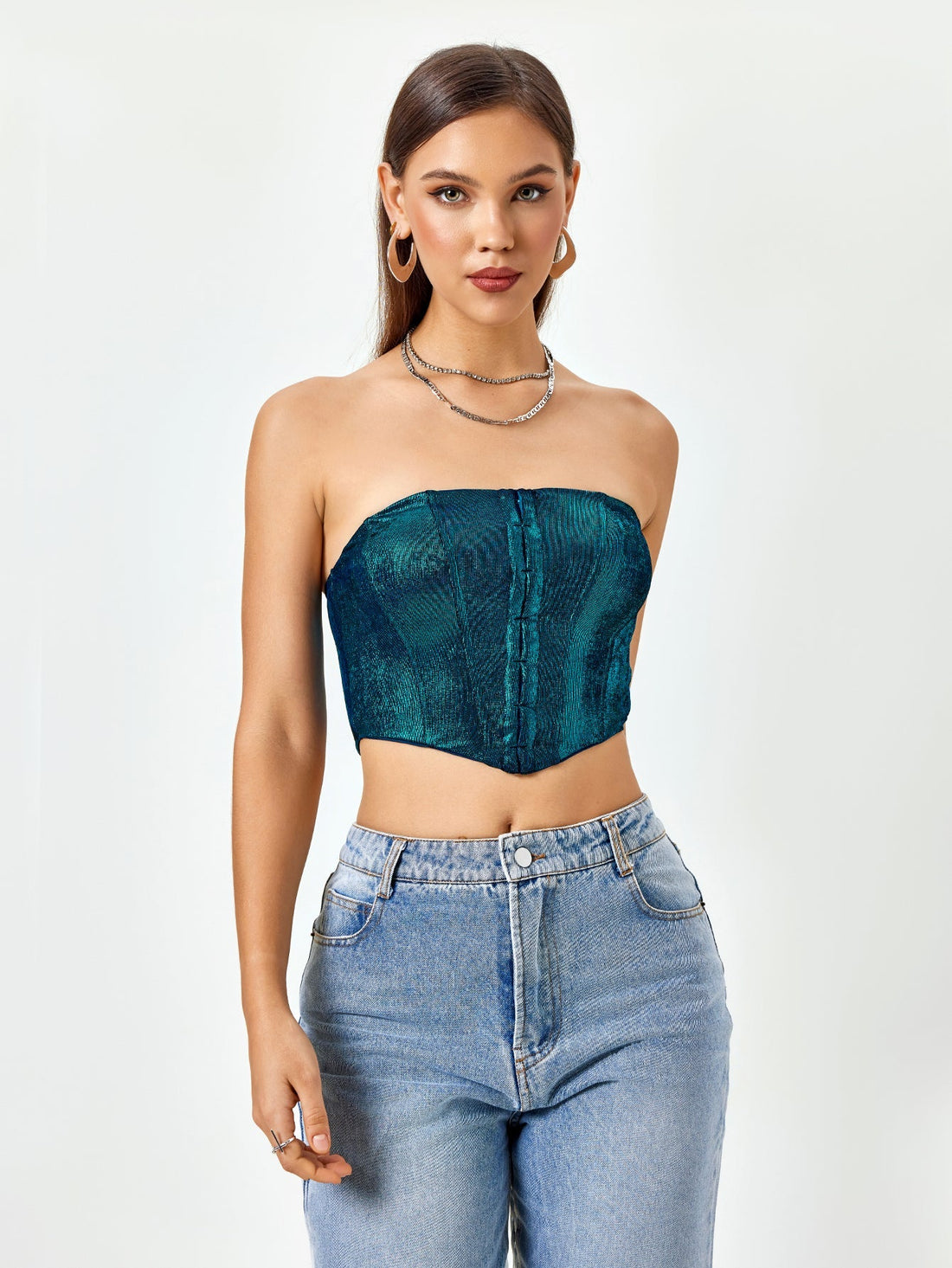 Woman wearing a teal textured metallic strapless corset top and light wash denim jeans