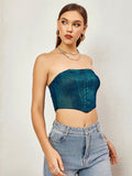 Woman in teal textured metallic strapless corset top and light wash denim jeans, side profile