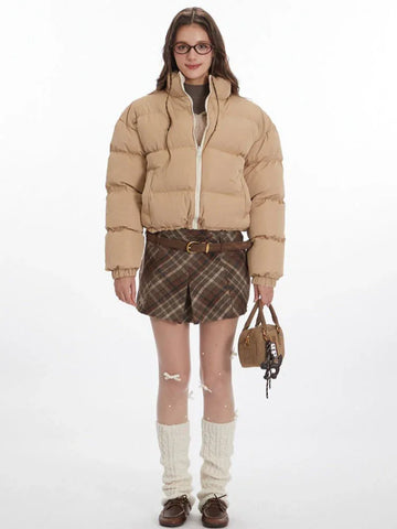 Woman wearing a beige cropped puffer jacket with a white zipper and stand-up collar.
