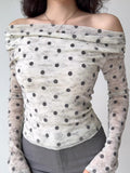 Model showcasing a fitted polka dot sheer mesh top with an off-the-shoulder design and long sleeves.