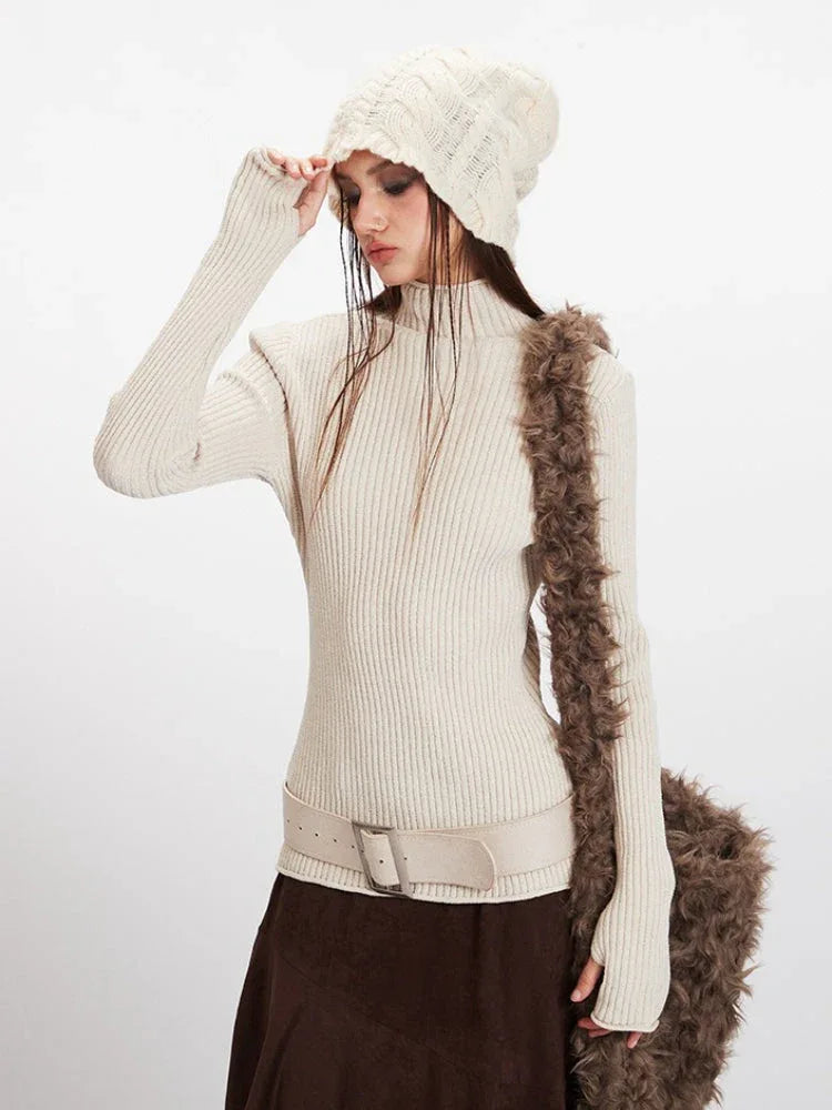 Close-up of a woman wearing a cream ribbed knit turtleneck sweater, a cream textured knit beanie, and a cream leather belt.