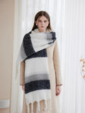 Woman styled with a beige coat and a thick, striped scarf featuring white, grey, and dark blue stripes