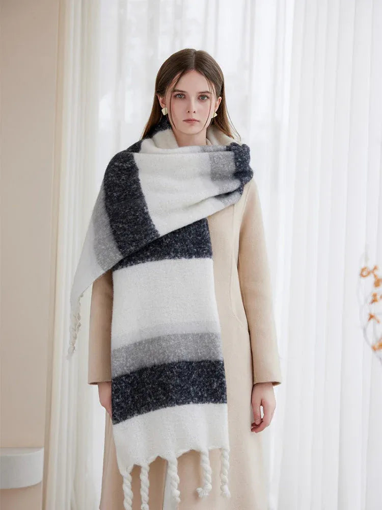 Woman styled with a beige coat and a thick, striped scarf featuring white, grey, and dark blue stripes