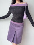 Full body shot of a woman in a grey and purple off-the-shoulder top and a purple skirt, accessorized with a purple handbag and necklace.
