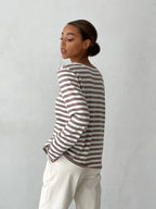 Side view of a woman wearing a striped long-sleeve top and cream trousers, with her hair in a bun.