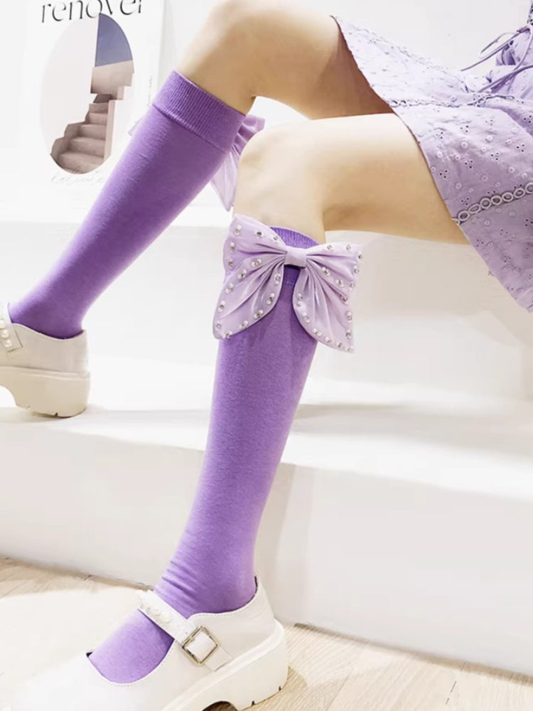 Purple knee-high socks with large decorative bows adorned with pearl-like accents on the calf.
