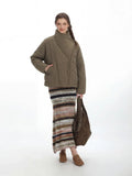 Full-length view of a woman in a cropped olive green quilted jacket and a striped maxi skirt.