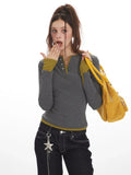 Close-up of a woman wearing a grey long-sleeve Henley top with contrast green cuffs and hem, and dark wash baggy jeans