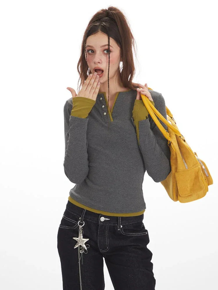 Close-up of a woman wearing a grey long-sleeve Henley top with contrast green cuffs and hem, and dark wash baggy jeans